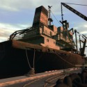 A large ship moored at the docks with some builders nearby.